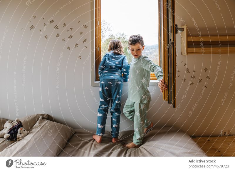 Siblings in pajamas looking out window sibling children childhood observe curious bedroom morning spare time cellphone kid domestic girl brother sister boy