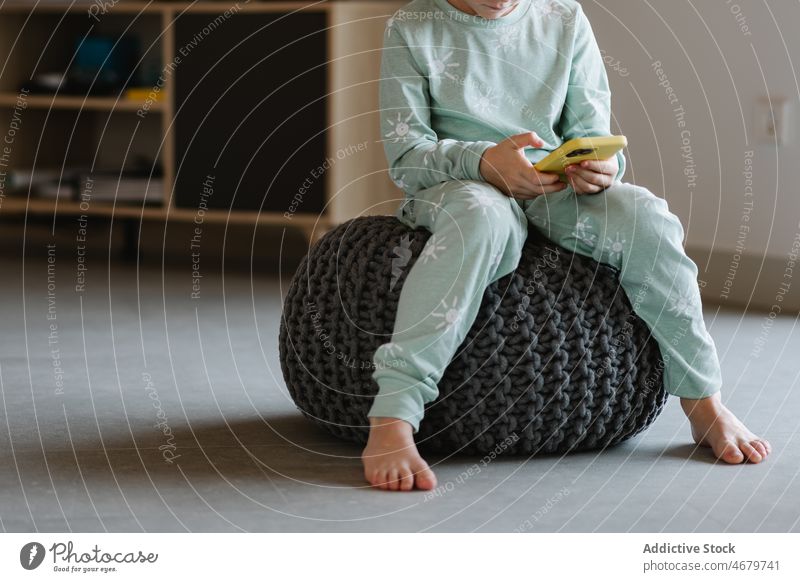 Anonymous boy in pajama playing on smartphone kid childhood videogame pastime morning domestic room apartment adorable barefoot flat cute home residential