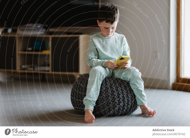 Boy in pajama playing on smartphone boy kid childhood videogame pastime morning domestic room apartment adorable barefoot flat cute home residential nightwear