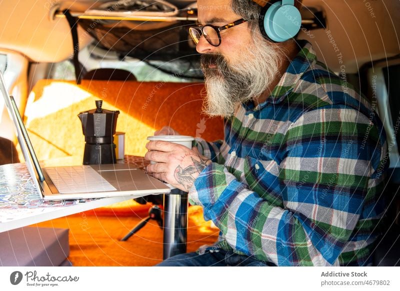 Elderly man watching video on laptop in camper elderly mature headphones traveler road trip van browsing online device gadget netbook using surfing remote