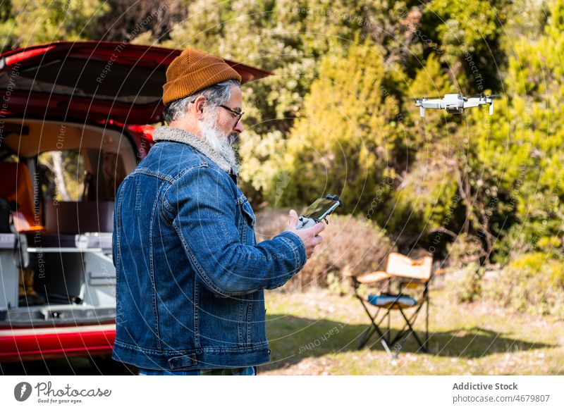 Elderly man controlling drone in countryside remote control operate uav elderly camper forest mature traveler van trip male beard caravan road trip aircraft