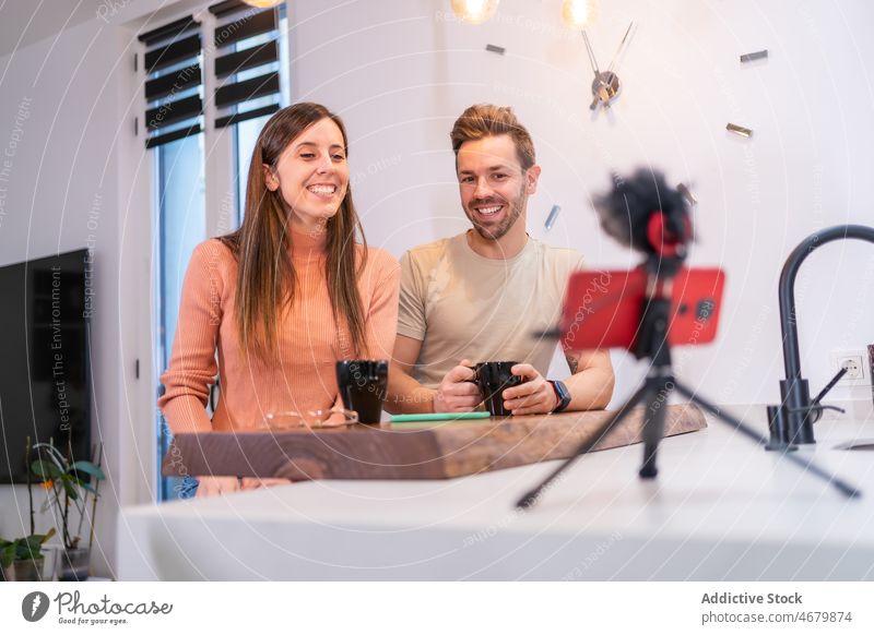 Cheerful couple recording vlog while drinking coffee kitchen blogger smartphone social media internet caffeine hot drink counter relationship beverage bonding