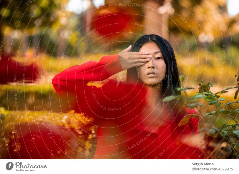 Portrait of an East Asian woman wearing a red suit and covering her eye with a hand in a garden elegant posing east asian spain flowers park stylish attractive