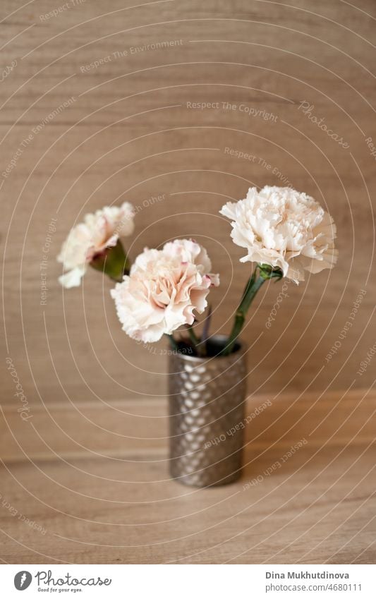 Three peach color carnations bouquet in a small vase on wooden table isolated. Floral vertical backdrop. Romantic surprise for a birthday or wedding. floral