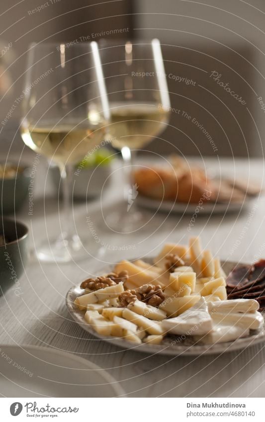 Delicious gourmet cheese platter and two white wine glasses on the table. Cheese collection or various types. Cheese and cold cuts selection. Appetizers and wine romantic date dinner.