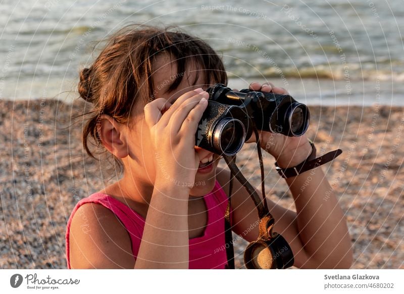 Tanned toddler girl with brown hair on the beach in summer looking through binoculars sunset child cute happy holiday kid sea smile travel vacation young
