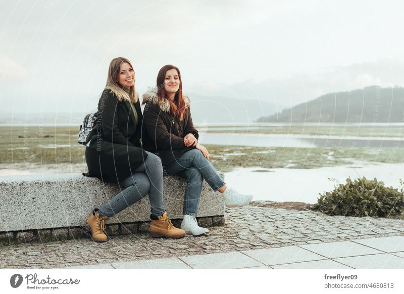 Two female friends sitting on a bench tourists landscape winter cold wetland galicia spain swamp contemplating calm background weather blue green hiking hike
