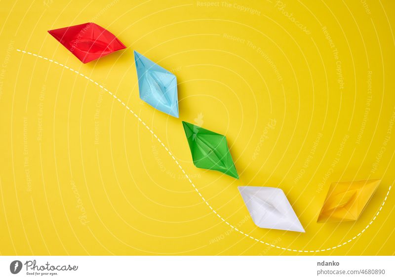 multi-colored paper boats follow the leader on a yellow background. The concept of manipulation of the masses, the path for a strong leader above association