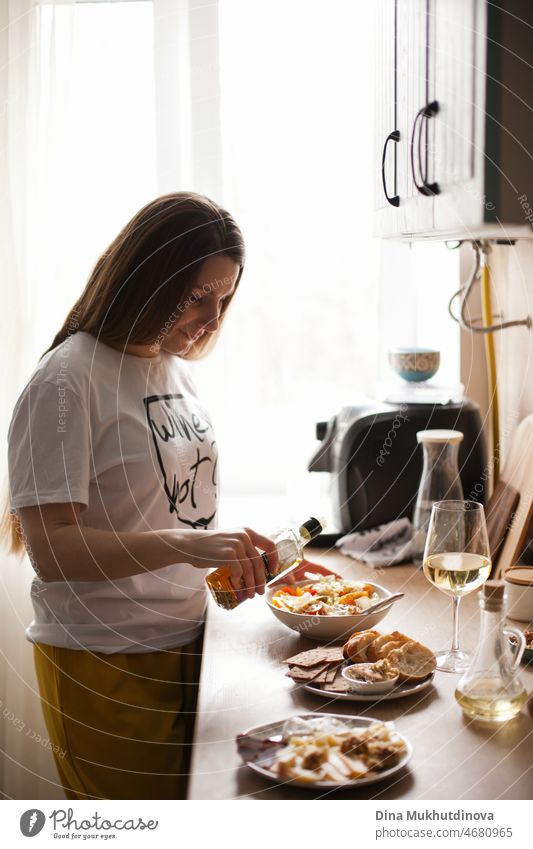 Woman cooking dinner at home and drinking white wine. Young woman cooking salad for lunch or dinner and preparing appetizers.  Woman in the kitchen, cooking. Food and drink.
