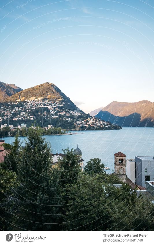 Lake in front of mountains and village in evening mood Moody Shadow Mountain Lugano Lake Lugano Church Village Vantage point Blue sky Switzerland Ticino