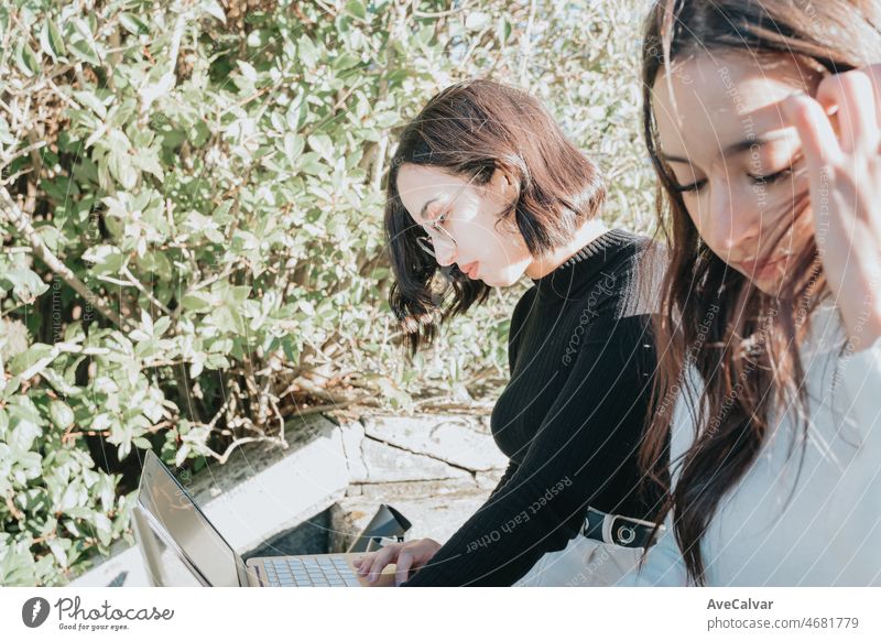 Two young woman student working on laptops outdoors. Concentration and hard working to archive good marks on exams. Last minute study. Young and new at the university concept.