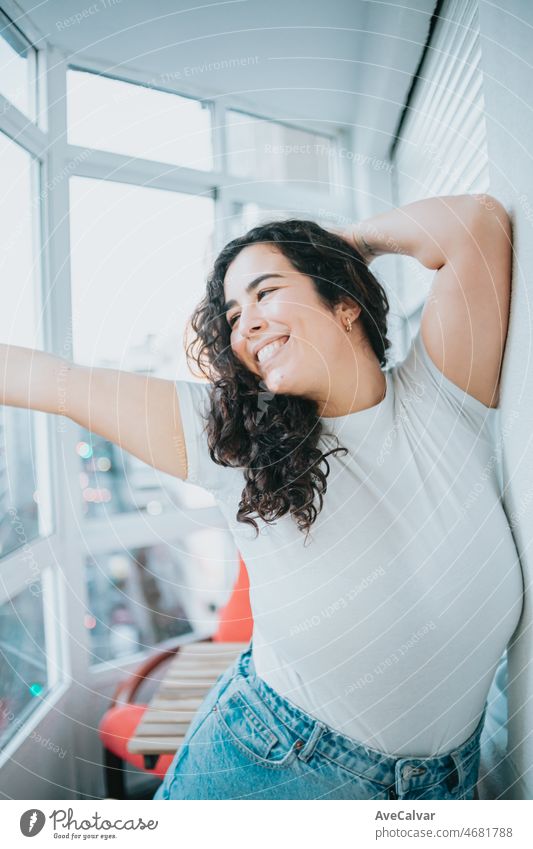 Young woman smiling happily while dancing with long curly hair, hispanic culture. New at the city, new home moving concept. City lifestyle on modern clothes