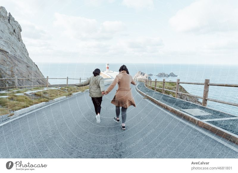 Vintage film image of two young women walking towards a lighthouse on the coast with soft tones. Spring ambient freedom and liberty concepts. Friendship and road trip vibes