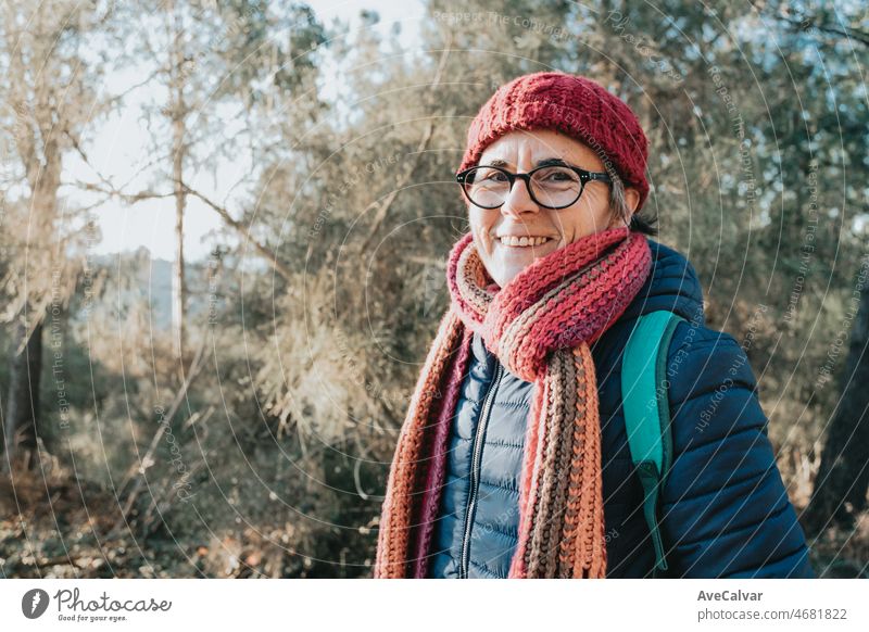 Old woman on winter clothes and hat smiling during a day outdoors. Senior people activities on nature during the sunset. Mental health grandmother concept