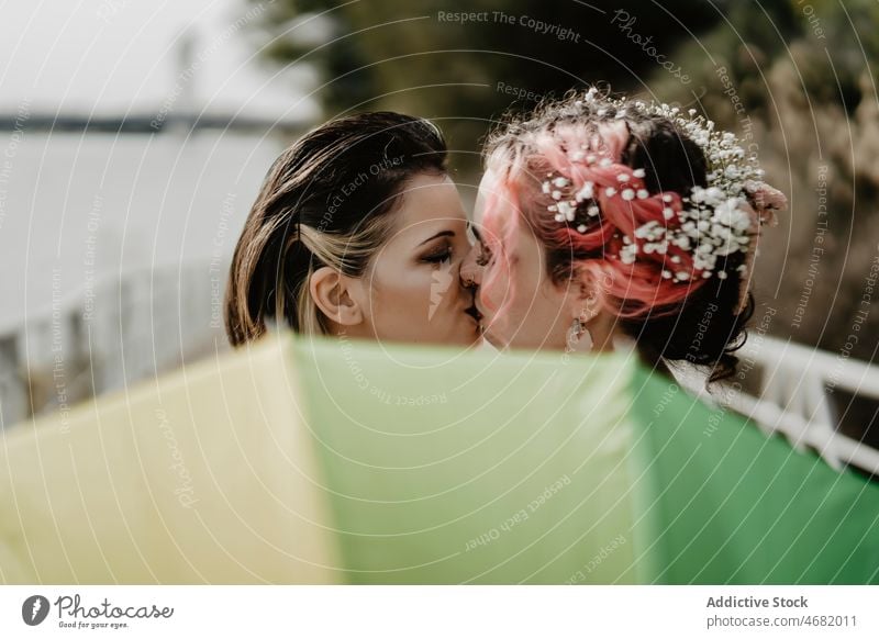 Brides kissing behind umbrella during wedding women bride love lesbian couple park celebrate female together romantic bridal happy daytime partner girlfriend