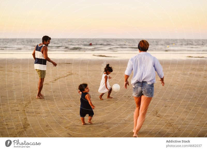 Cheerful diverse family playing with ball on beach father mother multiethnic children boy girl son game sister having fun multiracial football sibling childhood