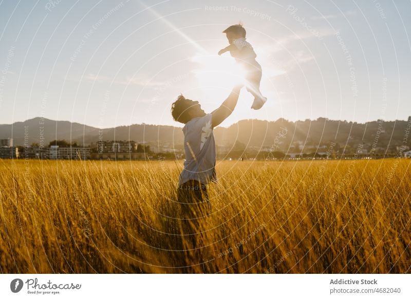 Anonymous man spending time with little son in yellow field dad father toddler kid having fun toss countryside meadow grass child male rural parent carefree