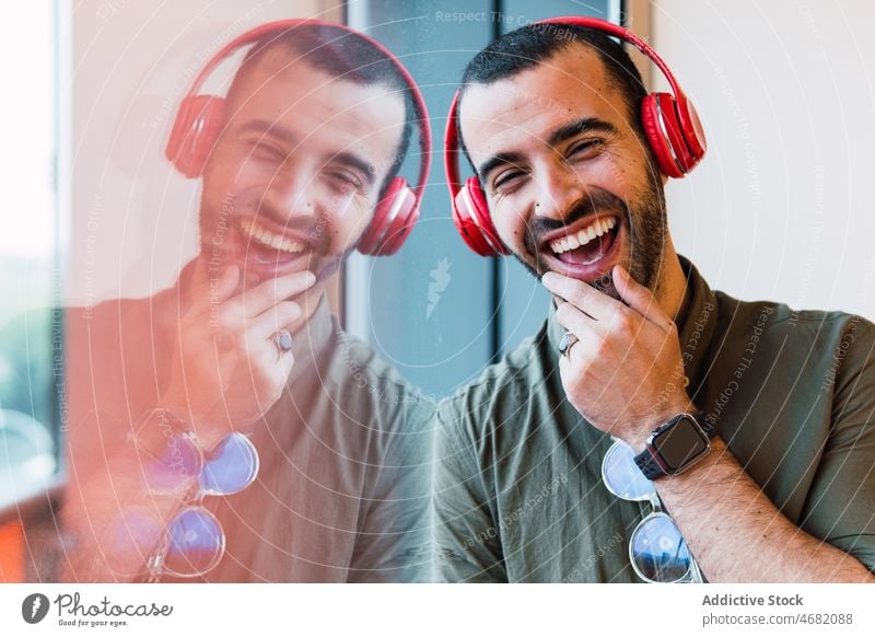 Cheerful man listening to music near window headphones song pastime leisure meloman hobby male happy cheerful room device reflect reflection glass sound light