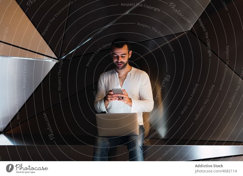Man with laptop browsing smartphone in studio man futuristic 3d text message modern design online internet male guy gadget using device dark mobile wall dim app