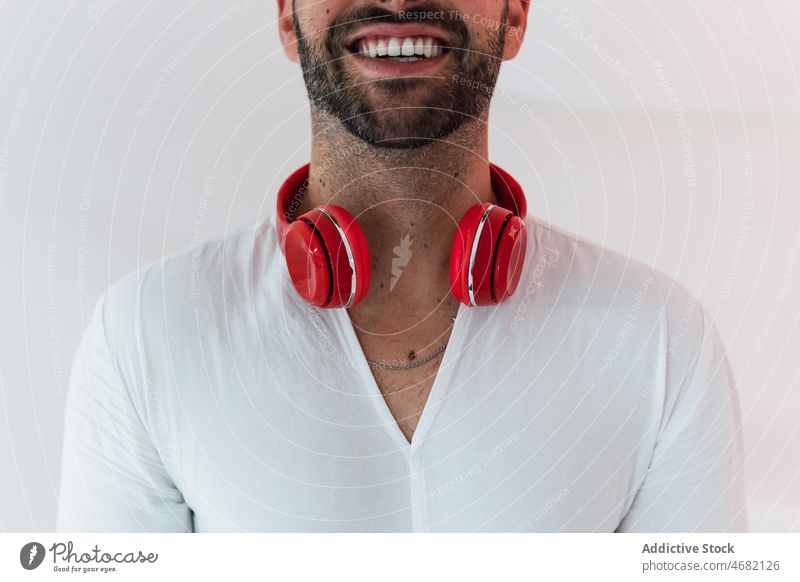 Anonymous cheerful man listening to music white background headphones song pastime leisure meloman hobby male happy room device sound light wireless beard smile