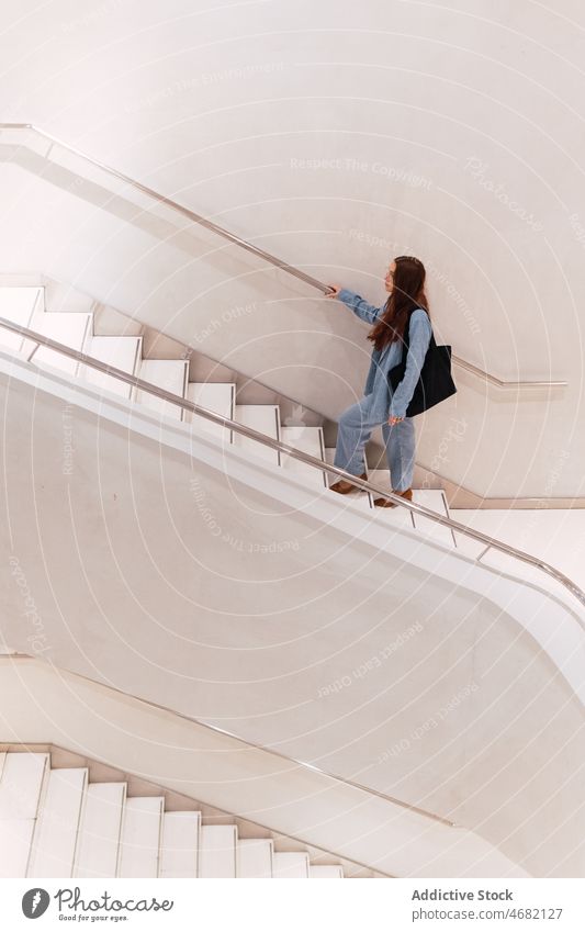 Unrecognizable woman walking on stairs staircase upstairs stairway elegant style design corridor hall fashion female trendy hallway long hair handbag spacious