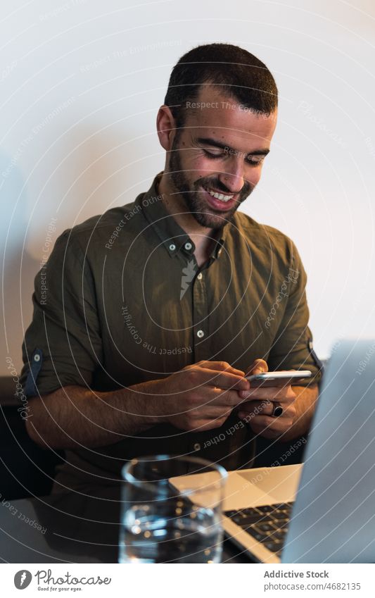 Happy man browsing smartphone near laptop online internet smile work workplace modern glad delight text message remote happy workspace netbook male table device
