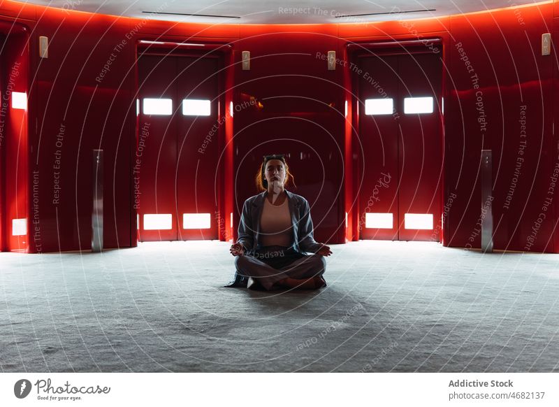Woman meditating in foyer with elevators woman lobby lotus pose zen lift meditate stress relief obscure design feminine glow dark red spacious trendy modern dim