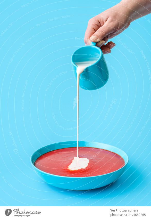 Pouring cream in tomato soup minimalist on a blue background bowl close-up color copy space cuisine delicious dinner drip food gazpacho gourmet hand healthy hot