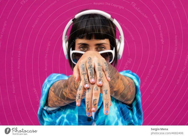 Attractive woman with headphones showing the tattoos on her hands on a pink background charismatic brunette young bright blue shirt studio sexy female model