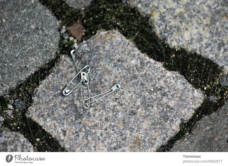 Lost for sure Safety pin Metal interconnected Doomed Paving stone interstices Detail Colour photo Deserted lost property