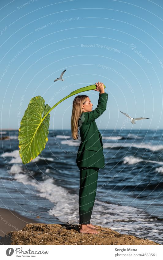 Fine art photography of an elegant Caucasian woman on the beach with a large green leaf artistic Artist Peace Water barefoot Spain Europe plant clear blue sky