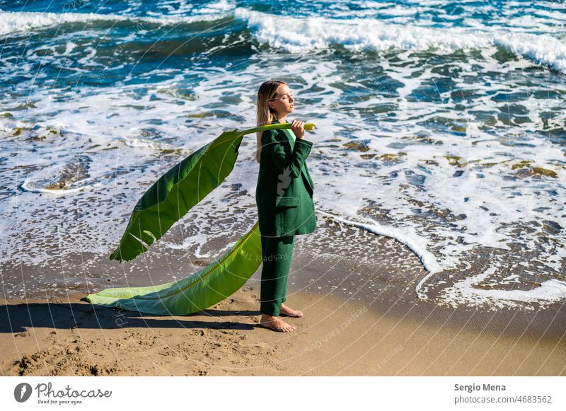 Artistic photography of an elegant Caucasian woman on the beach with a large green leaf closeup girl blond pretty beautiful attractive standing leaves sea ocean