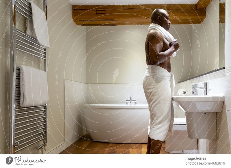 Man of African ethnicity wrapped in a towel, in a modern bathroom adult african afro american background beauty black body bodycare brown clean cleanliness