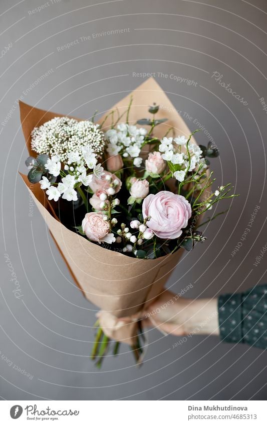 Hand holding bouquet of pink and white flowerson wooden table at flower shop. Floristics and selling flowers small business. Pink fresh spring floral background with copy space on light gray background.