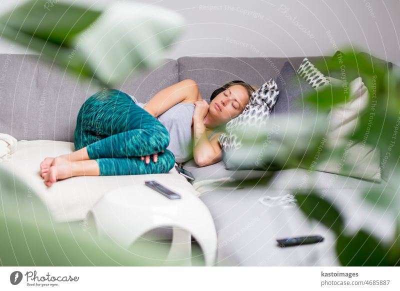 Young casual woman lying on couch cushion with eyes closed, relaxing on cozy sofa pillow, relaxed girl taking nap at home, wearing headphones, listening to music or podcast