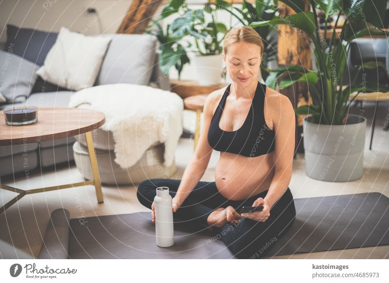 Young happy and cheerful beautiful pregnant woman chating to family and friends on mobile phone while staying fit, sporty and active on her maternity leave. Pregnancy, yoga concept
