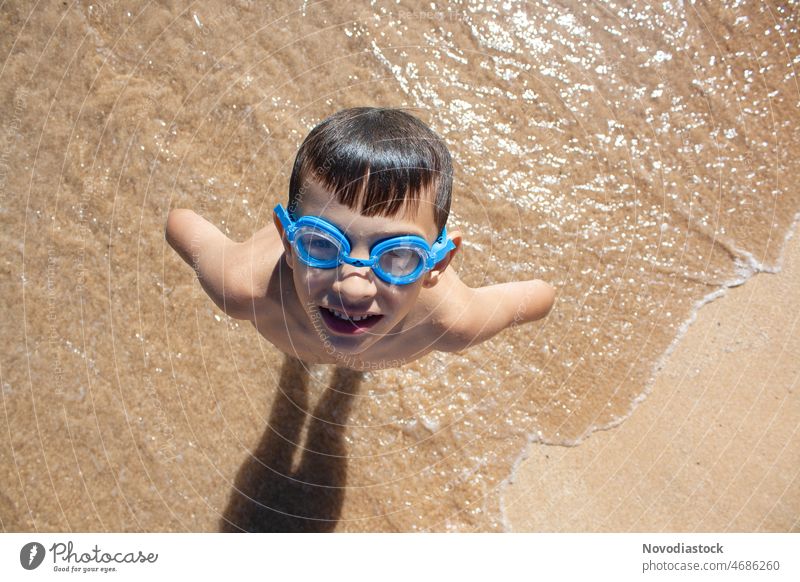 Portrait of a caucasian 6 year old boy on the beach wearing goggles, image taken from the top, summer holidays concept portrait soggles top view isolated Summer