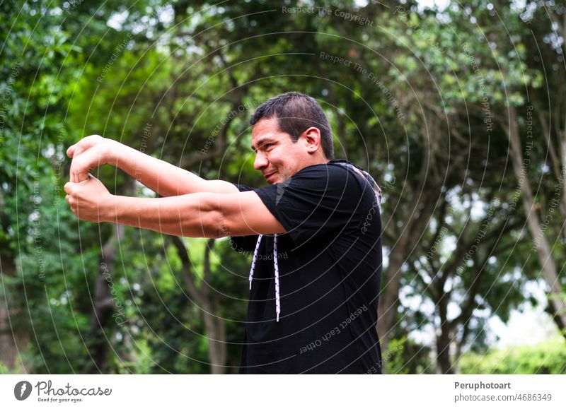young peruvian man warming up by stretching arms before exercise. workout exercising cardio face person sport fitness summer nature sun park lifestyle male
