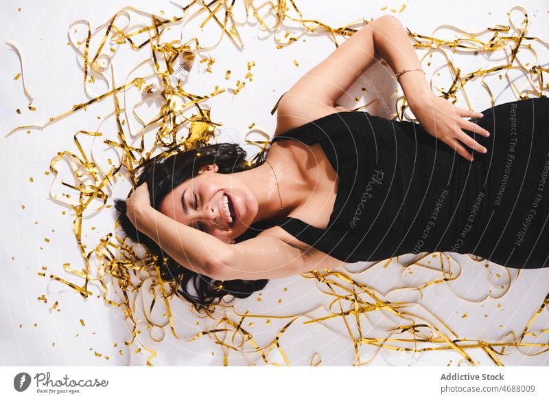Laughing woman lying with confetti on floor birthday celebrate holiday style event festive tinsel decoration smile fashion dress female happy occasion optimist