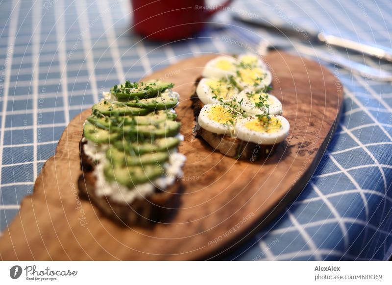 Two slices of bread - one with avocado and one with egg - on an olive wood board on a breakfast table Avocado Egg boiled egg Bread Black bread Bread and butter
