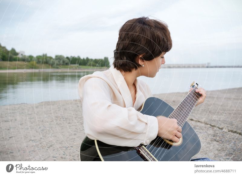 Young female musician playing guitar on a beach sound woman people sitting guitarist caucasian young person portrait girl instrument shore holding lifestyle sea
