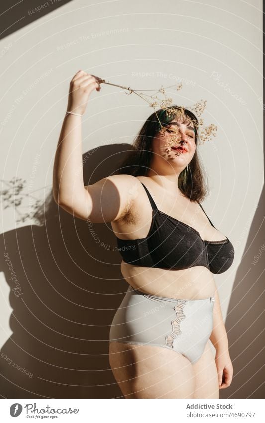 Overweight woman in underwear with dried flowers plus size twig figure sunlight smile lingerie room enjoy feminine eyes closed delight home content female body
