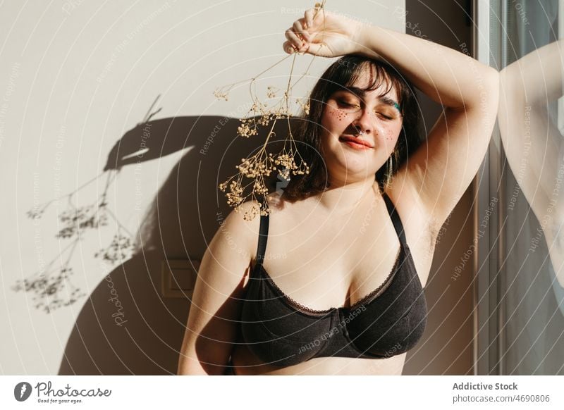 Overweight woman in underwear with dried flowers plus size twig figure sunlight smile lingerie room shadow enjoy feminine makeup windows delight home content