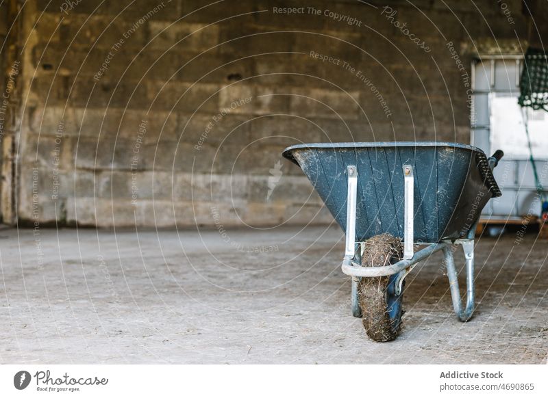 Wheelbarrow placed in rural area wheelbarrow countryside shabby weathered barn equipment cart rustic appliance shed stone wall dirty construction aged obsolete