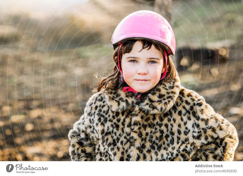 Girl in helmet standing in countryside girl kid outerwear rural appearance childhood leisure pastime warm clothes protect coat fur style charming safety cute