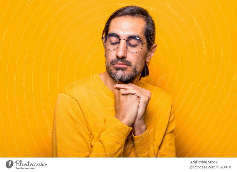 Peaceful man with closed eyes style tranquil dreamy peaceful appearance mood hope hopeful calm studio eyeglasses eyes closed light hands clasped beard male