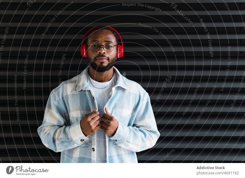 Black man in headphones and jacket meloman music street song city wall stylish african american black male guy style trendy building beard wireless listen