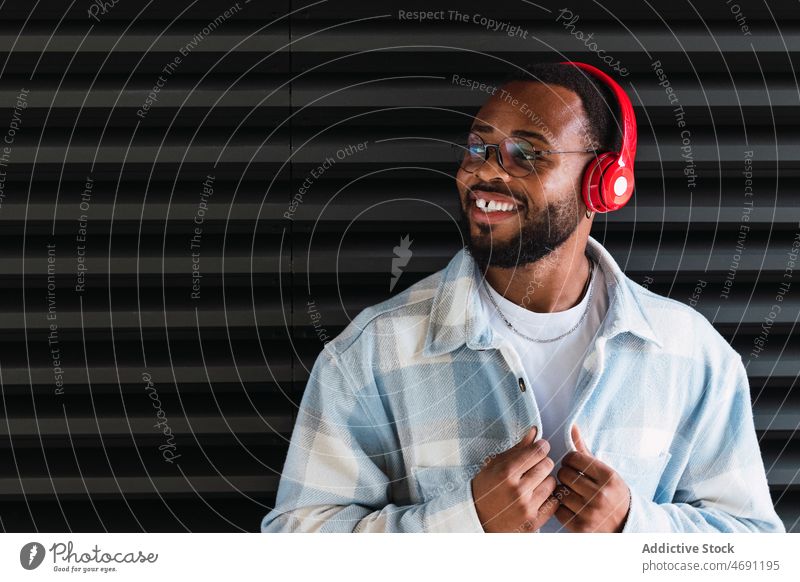 Smiling black man in headphones and jacket meloman music cheerful street song city wall stylish smile african american happy male guy style trendy building