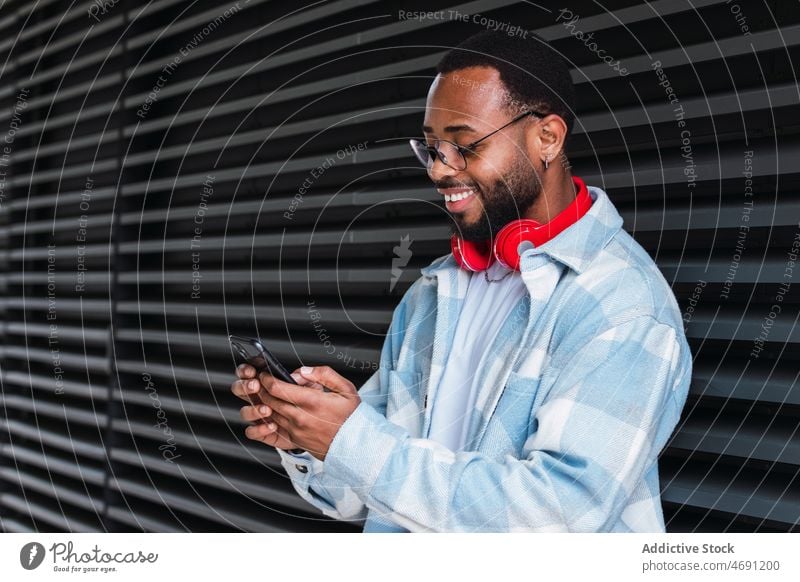 Cheerful black man with smartphone listening to music headphones meloman song street city pastime leisure building african american text message male device
