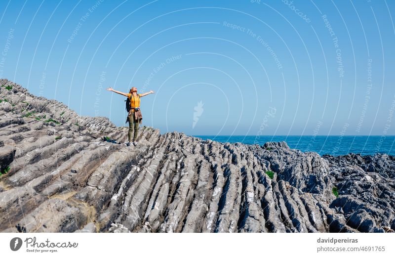 Young woman raising arms hiking through flysch rock landscape backpack copy space freedom young adult walking carefree trekking seascape people nature camera